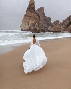 a woman in a white dress walking on the beach with her back to the camera