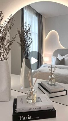 a white table topped with two vases filled with flowers and reeds next to a mirror