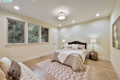 a large bedroom with white walls and wood flooring, along with a bed in the center