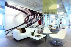 the interior of a hair salon with chairs, tables and couches in front of a large wall mural