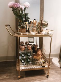 a gold bar cart filled with lots of bottles and glasses on top of a hard wood floor