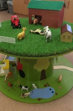 there are many toy farm animals on the green table top with fake grass and toys in the background