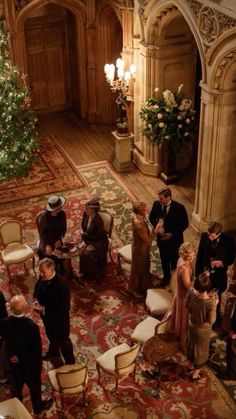 a group of people standing around a living room next to a christmas tree in a building