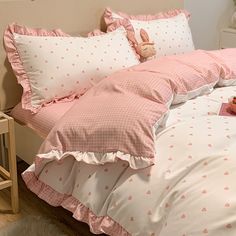 a bed with pink and white polka dot comforter, pillows and stuffed animals on it