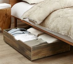 an open drawer underneath a bed with white fur on the top and bottom sheets in it