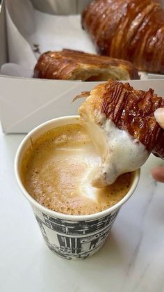 a person is dipping some food into a coffee cup with croissants in the background