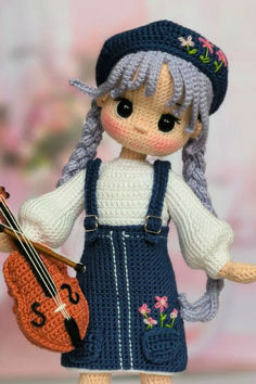 a crocheted doll holding a violin and wearing a knitted hat with flowers on it