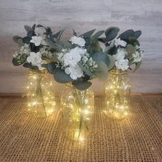 three vases with flowers and lights are sitting on a table