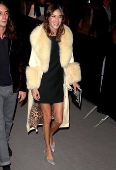 a woman in a short black dress is walking next to a man wearing a fur coat