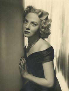 an old black and white photo of a woman leaning against a wall with her hands on her chest