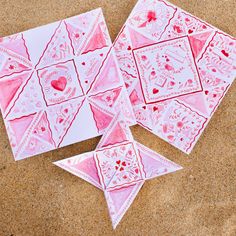 three pink and white cards with hearts on them sitting in the sand next to each other