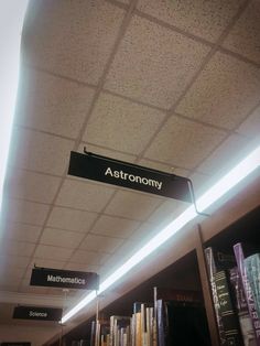 a sign that reads astronomy hangs from the ceiling in a library with bookshelves