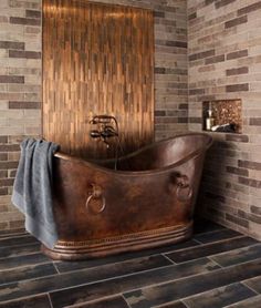 an old fashioned copper bathtub in front of a brick wall and tiled flooring