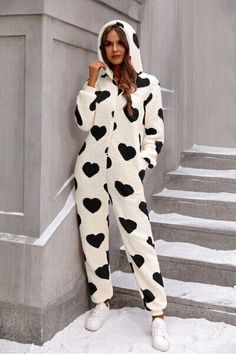 a woman in a cow print jumpsuit leaning against a wall with her hand on her head