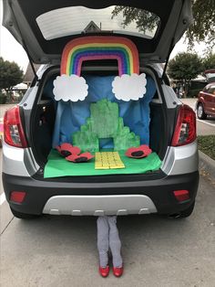 a child standing in front of the trunk of a car that has been decorated with rainbows and clouds