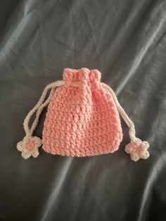 a pink crocheted bag sitting on top of a gray sheet with two white pom poms