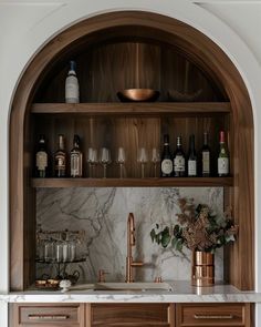 a kitchen with marble counter tops and wooden cabinets, wine glasses on the shelf above the sink