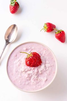 a bowl of oatmeal with strawberries and spoons next to it