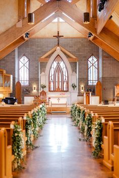 the inside of a church with pews and flowers on the aisle, decorated with greenery