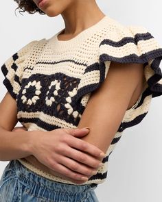 a woman with her arms crossed wearing a knitted sweater and denim shorts, standing against a white background