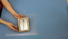 a person holding a piece of wood in front of a blue table with a mirror on it