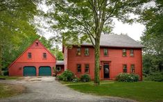 a red house with two garages in front of it and trees around the driveway