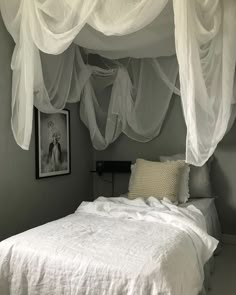 a white bed sitting under a canopy in a bedroom next to a wall with pictures on it