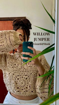 a woman taking a selfie in front of a mirror with her cell phone and wearing a crocheted sweater