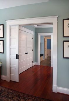 an empty room with two white doors and pictures on the wall above it, along with hardwood flooring