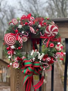 a christmas wreath with candy canes and greenery hanging on a wooden fence post