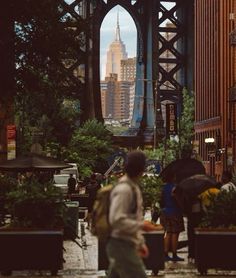 people are walking on the sidewalk under an overpass with buildings in the background,