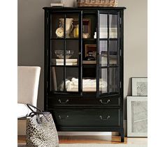 a black china cabinet with glass doors and leopard print bag on top, next to a white chair