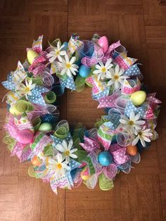 a colorful wreath with flowers, eggs and bows on the front of a wooden floor