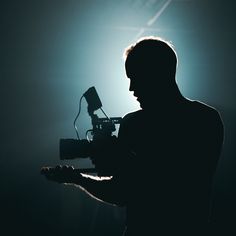 the silhouette of a man holding a camera in front of a light that is shining on him