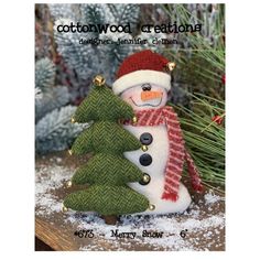 a small snowman next to a christmas tree in front of some pine trees with the words cottonwood creations written on it