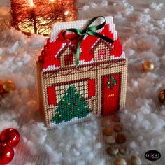 a small red house with a christmas tree on it and other ornaments around it in front of a lit candle