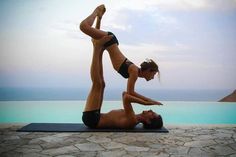 a man and woman doing yoga in front of a pool with the ocean behind them