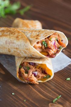 two burritos with meat and vegetables on a cutting board next to cilantro