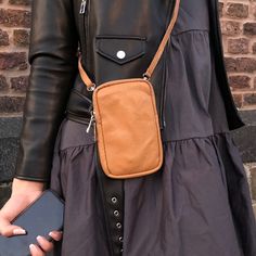 a woman in a black dress holding a cell phone and wearing a brown leather cross body bag