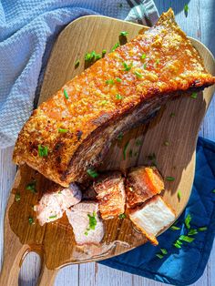 a large piece of meat on a wooden cutting board next to some bread and parsley