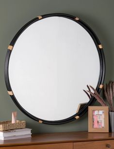 a round mirror sitting on top of a wooden dresser next to a potted plant