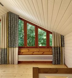 an empty room with wooden floors and curtains on the window sill, next to a radiator