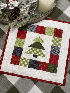 a quilted table runner with a candle and christmas decorations on it, along with pine cones