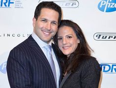 a man and woman standing next to each other in front of a red carpeted wall