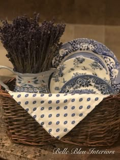 a wicker basket with lavenders and plates in it on a counter top next to a cloth napkin