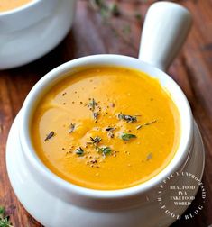 a white bowl filled with carrot soup on top of a wooden table next to a spoon