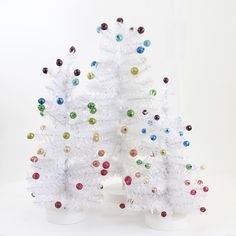 two white christmas trees decorated with multicolored ornaments