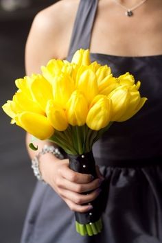 a woman in a black dress holding a bouquet of yellow tulips and pearls