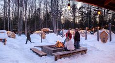 several people standing around a fire pit in the middle of some snow covered ground and trees