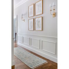 an empty hallway with white walls and wood flooring, framed pictures on the wall